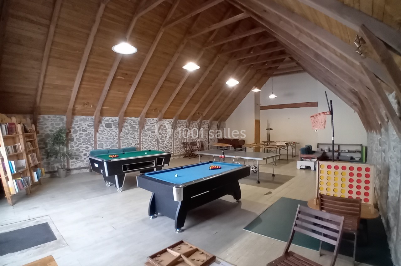 Salle de jeux avec billards, baby-foot, jeu de puissance 4 géant, étagères de livres et plafond en bois.