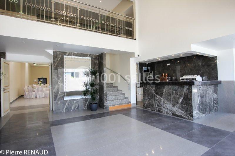 Hall d'entrée moderne avec comptoir en marbre, escalier, plantes décoratives et vue sur une salle de réception.