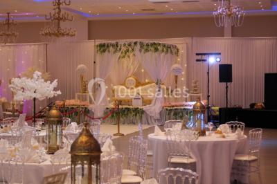 Salle de réception décorée avec une table dressée, un centre de table floral et une arche fleurie en arrière-plan.