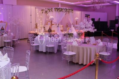 Salle de réception décorée avec une table dressée, un centre de table floral et une arche fleurie en arrière-plan.