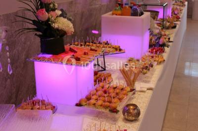 Salle de réception décorée avec une table dressée, un centre de table floral et une arche fleurie en arrière-plan.
