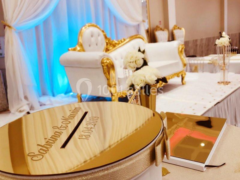 Boîte dorée gravée pour une cérémonie, avec un canapé blanc et doré en arrière-plan dans une salle décorée.