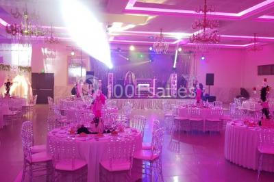 Salle de réception décorée avec une table dressée, un centre de table floral et une arche fleurie en arrière-plan.