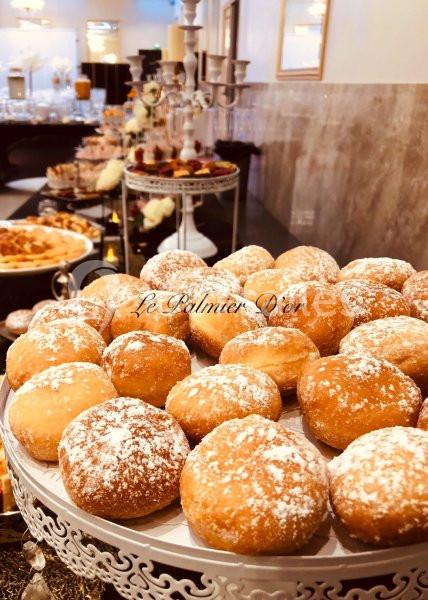 Plateau de beignets saupoudrés de sucre glace, présenté dans une salle de réception élégante avec un buffet en arrière-plan.