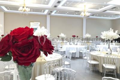 Salle de réception décorée avec une table dressée, un centre de table floral et une arche fleurie en arrière-plan.