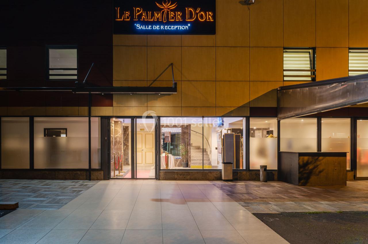 Façade éclairée d'une salle de réception avec enseigne ’Le Palmier d'Or’ visible au-dessus de l'entrée principale.