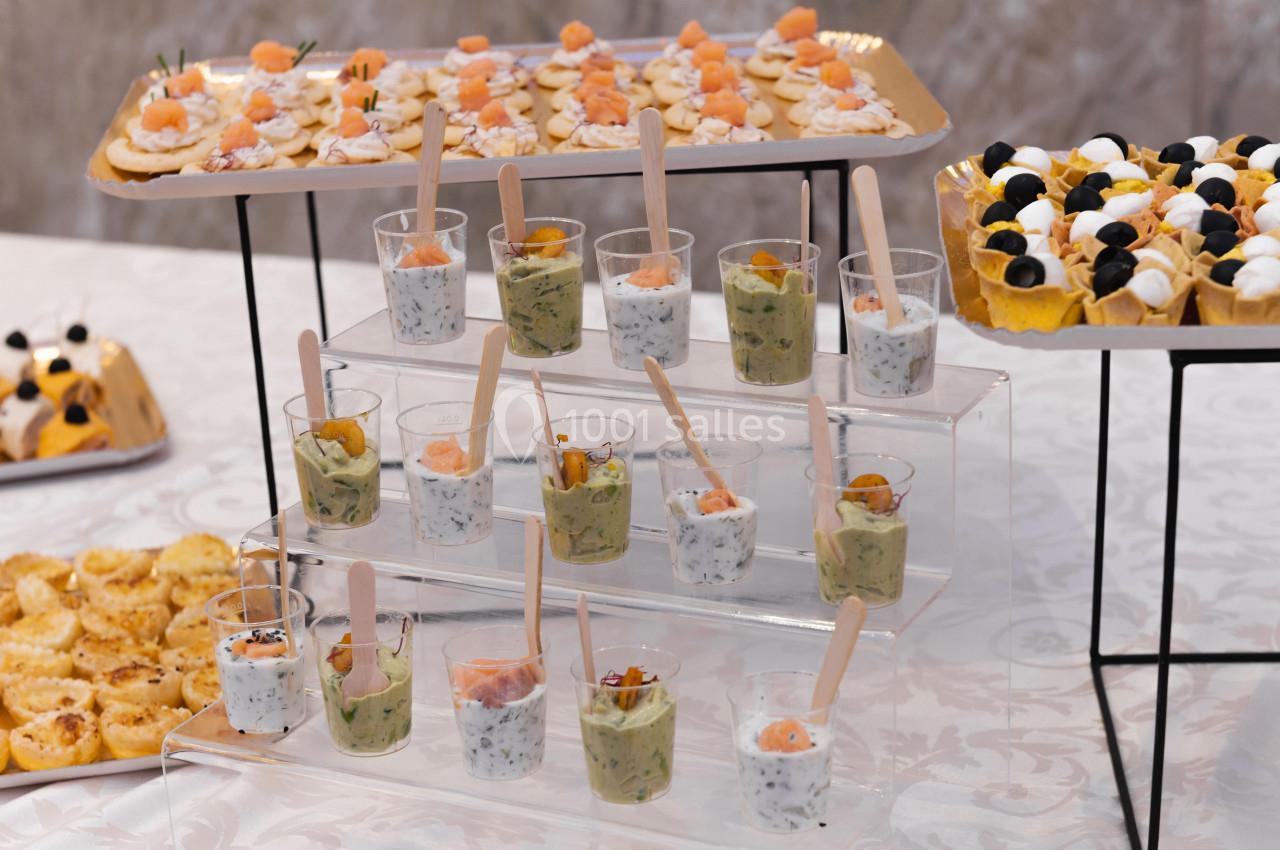 Buffet avec verrines salées, toasts au saumon, tartelettes et amuse-bouches variés sur une nappe blanche.