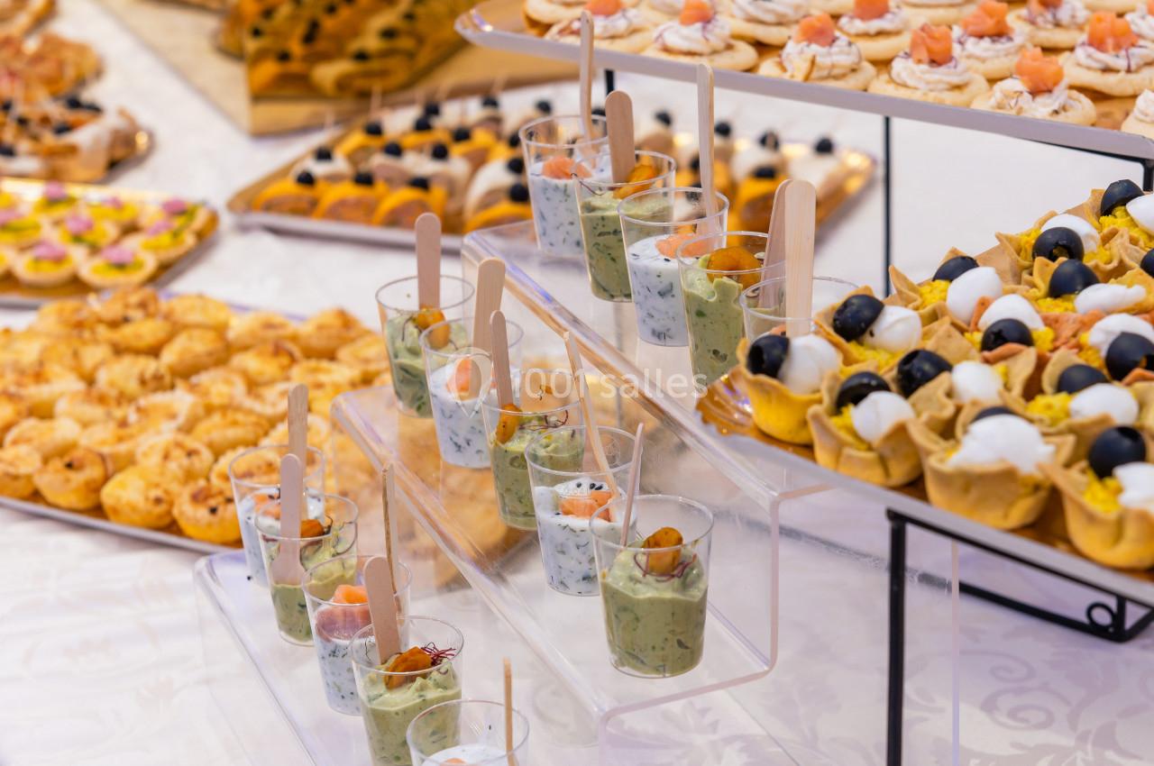 Buffet avec verrines salées, tartelettes garnies et autres amuse-bouches disposés sur des présentoirs.