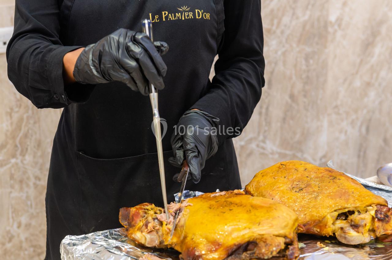 Personne en tablier noir découpant un gigot d'agneau rôti posé sur une table recouverte de papier aluminium.