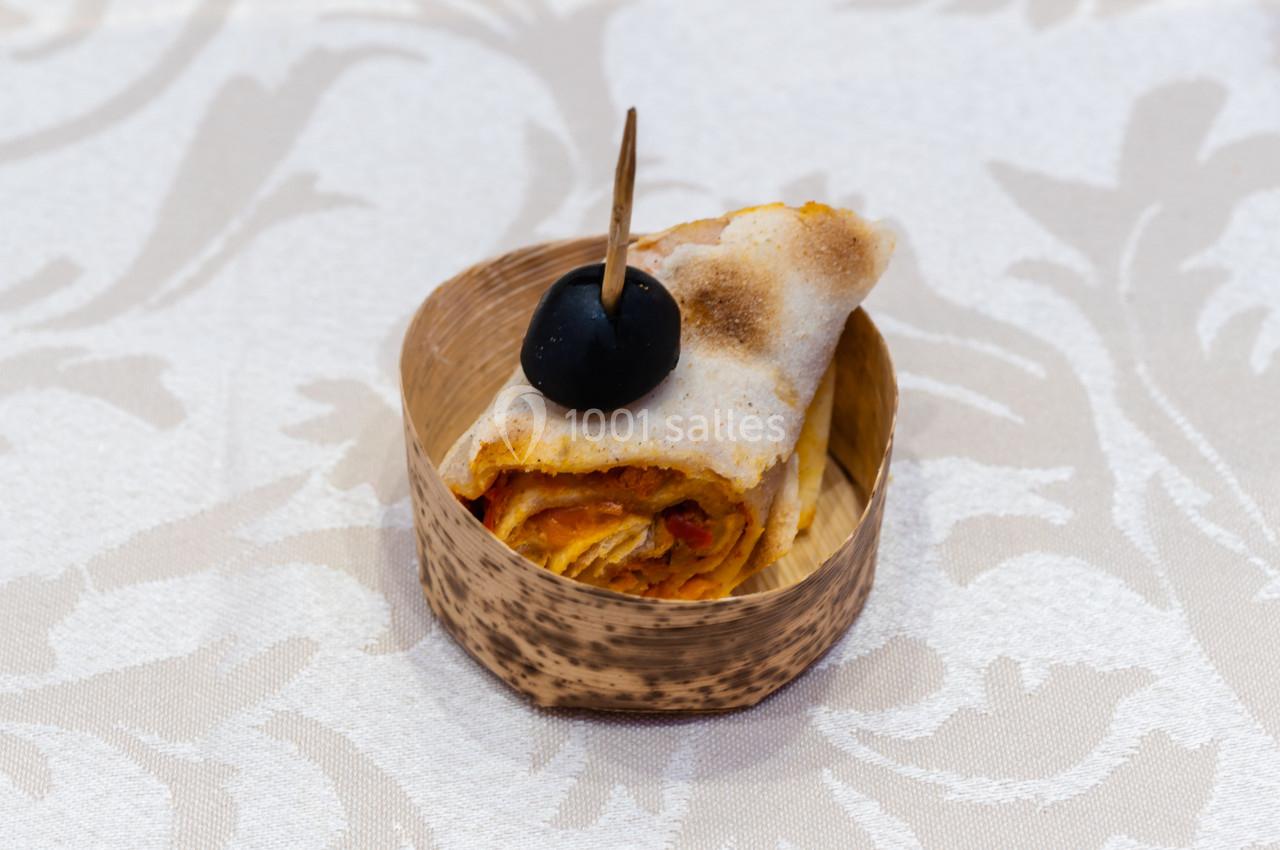 Rouleau de pâte garnie de sauce tomate et épices, surmonté d'une olive noire, présenté dans un récipient en bois.