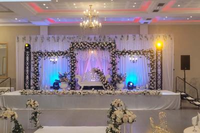 Salle de réception décorée avec une table dressée, un centre de table floral et une arche fleurie en arrière-plan.