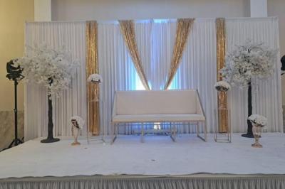 Salle de réception décorée avec une table dressée, un centre de table floral et une arche fleurie en arrière-plan.