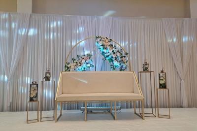 Salle de réception décorée avec une table dressée, un centre de table floral et une arche fleurie en arrière-plan.