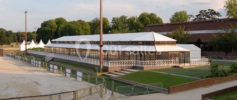 Location salle Rueil-Malmaison (Hauts-de-Seine) - Paris Country Club #26 Structure en toile blanche avec baies vitrées, entourée d'espaces verts et située près d'une carrière équestre.
