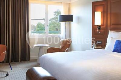 Miniature Location salle Rueil-Malmaison (Hauts-de-Seine) - Paris Country Club #32 Chambre d'hôtel lumineuse avec lit double, bureau bleu, fauteuil, télévision et balcon offrant une vue sur l'extérieur.