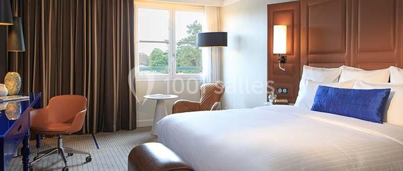 Location salle Rueil-Malmaison (Hauts-de-Seine) - Paris Country Club #32 Chambre d'hôtel lumineuse avec un grand lit, un bureau, un fauteuil, une table ronde et une fenêtre donnant sur un espace…