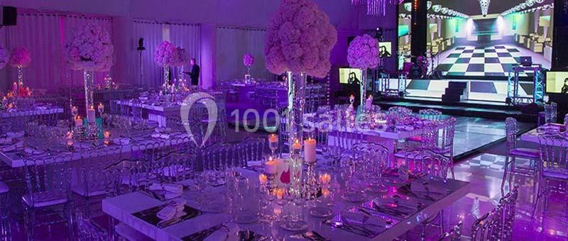 Location salle Rueil-Malmaison (Hauts-de-Seine) - Paris Country Club #22 Salle de réception décorée avec des tables élégantes, des chandeliers et un éclairage coloré, avec une scène en arrière-plan.