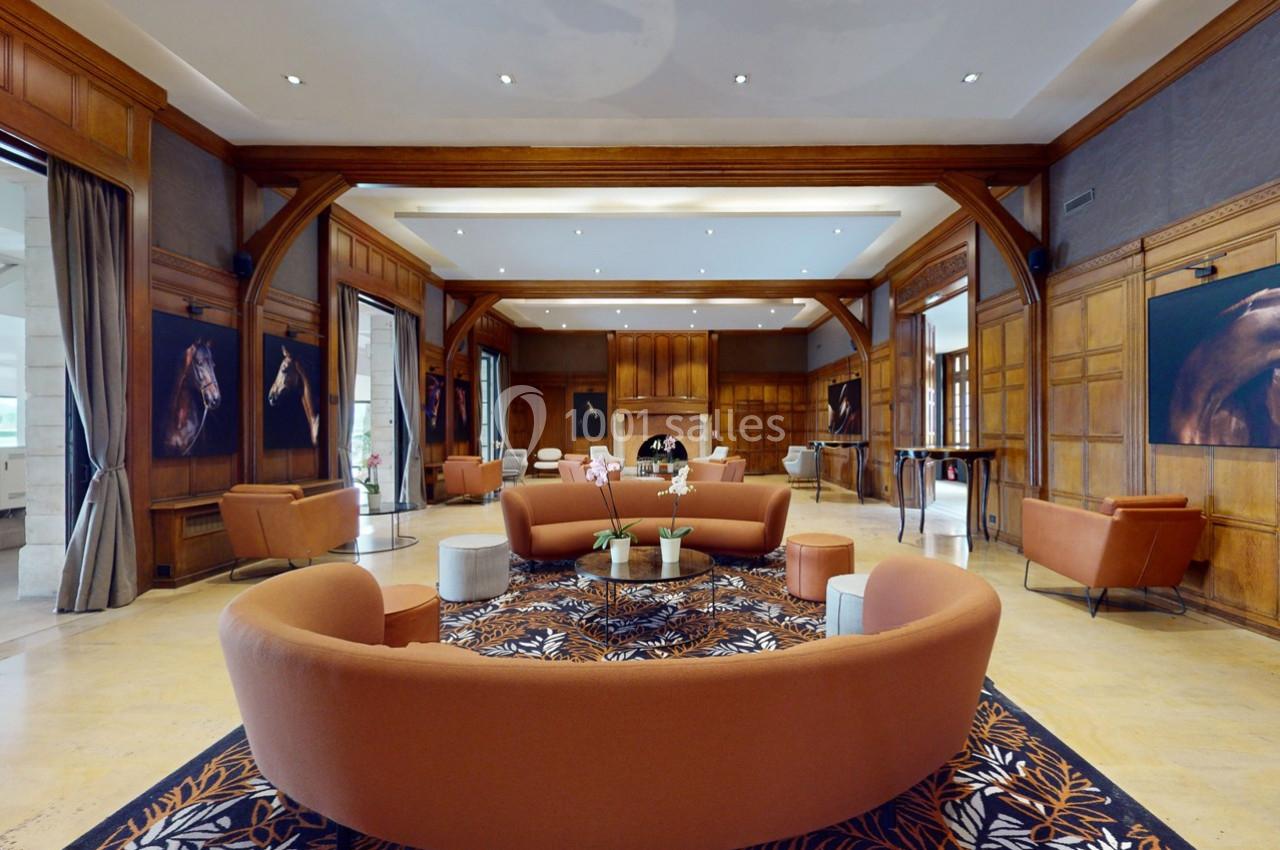 Location salle Rueil-Malmaison (Hauts-de-Seine) - Paris Country Club #13 Salon spacieux avec canapés orange, tapis floral, murs en bois et tableaux de chevaux accrochés.