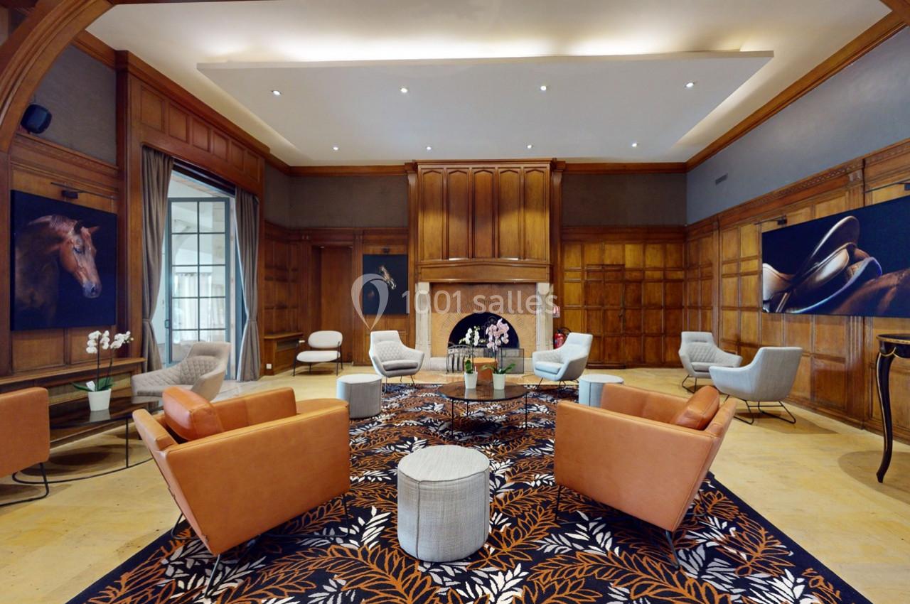 Location salle Rueil-Malmaison (Hauts-de-Seine) - Paris Country Club #15 Salle élégante avec fauteuils en cuir, tapis à motifs floraux, cheminée centrale et œuvres d'art sur les murs en bois.