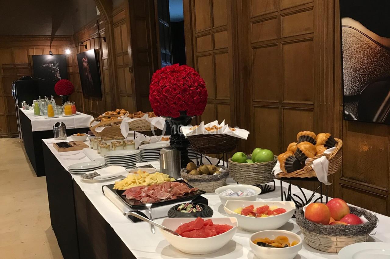 Location salle Rueil-Malmaison (Hauts-de-Seine) - Paris Country Club #16 Buffet avec viennoiseries, fruits frais, charcuterie, fromage et boissons disposés sur une table dans une salle en bois.