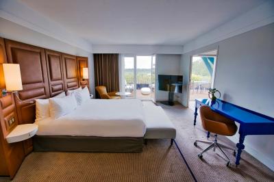 Miniature Location salle Rueil-Malmaison (Hauts-de-Seine) - Paris Country Club #33 Chambre d'hôtel lumineuse avec lit double, bureau bleu, fauteuil, télévision et balcon offrant une vue sur l'extérieur.