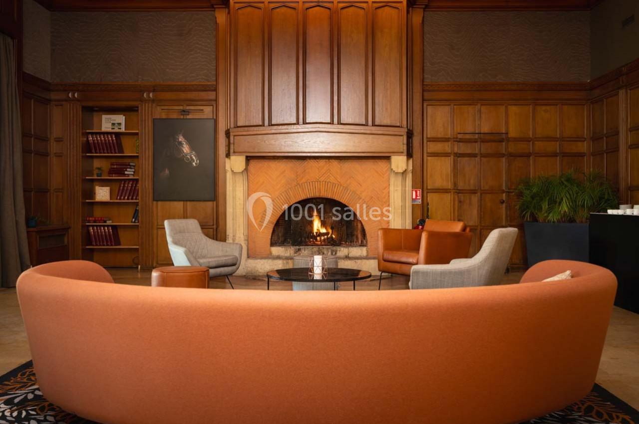 Location salle Rueil-Malmaison (Hauts-de-Seine) - Paris Country Club #14 Salon chaleureux avec cheminée allumée, fauteuils modernes, bibliothèque et plantes dans un décor en bois.