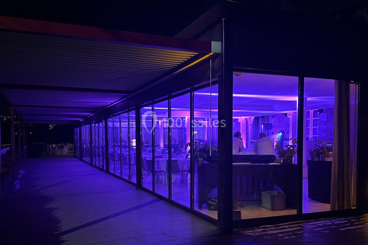 Location salle Rueil-Malmaison (Hauts-de-Seine) - Paris Country Club #29 Salle vitrée éclairée en violet la nuit, avec des tables dressées et des personnes à l'intérieur.