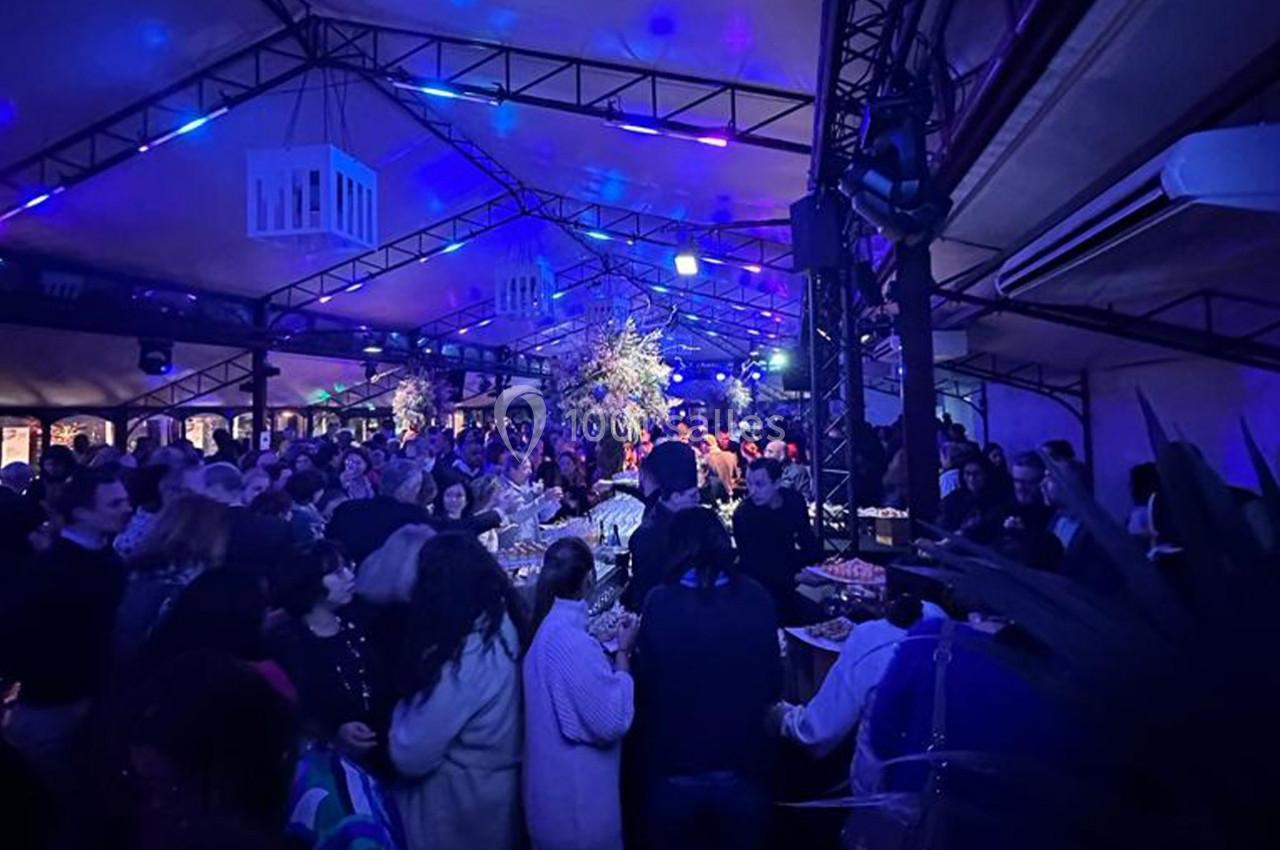 Location salle Rueil-Malmaison (Hauts-de-Seine) - Paris Country Club #30 Foule rassemblée dans un espace couvert illuminé de lumières bleues, autour de tables garnies de plats.
