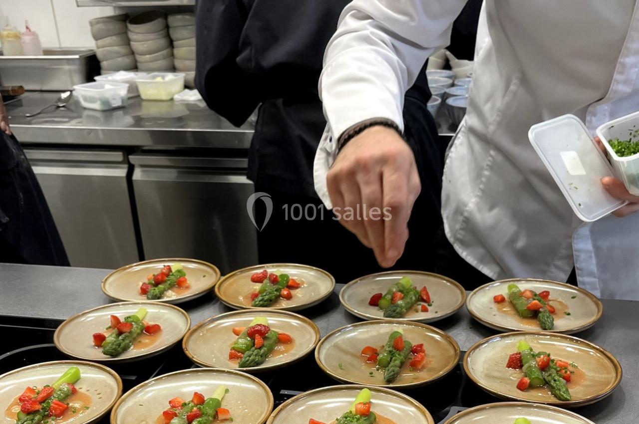 Location salle Rueil-Malmaison (Hauts-de-Seine) - Paris Country Club #28 Un chef dispose des assiettes garnies d'asperges, fraises et herbes dans une cuisine professionnelle.