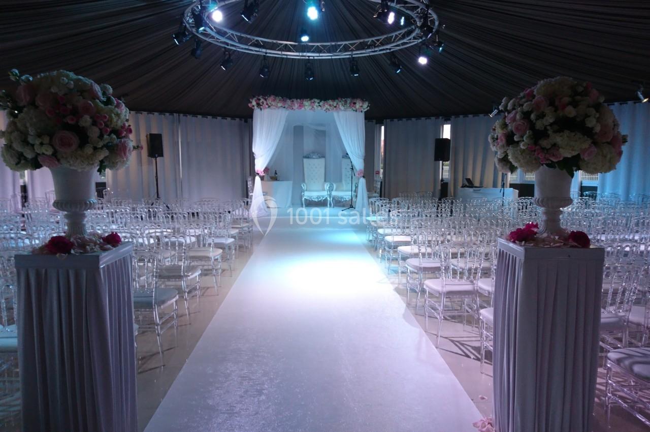 Location salle Rueil-Malmaison (Hauts-de-Seine) - Paris Country Club #25 Allée centrale décorée pour une cérémonie, entourée de chaises transparentes et ornée de fleurs sous une tente éclairée.