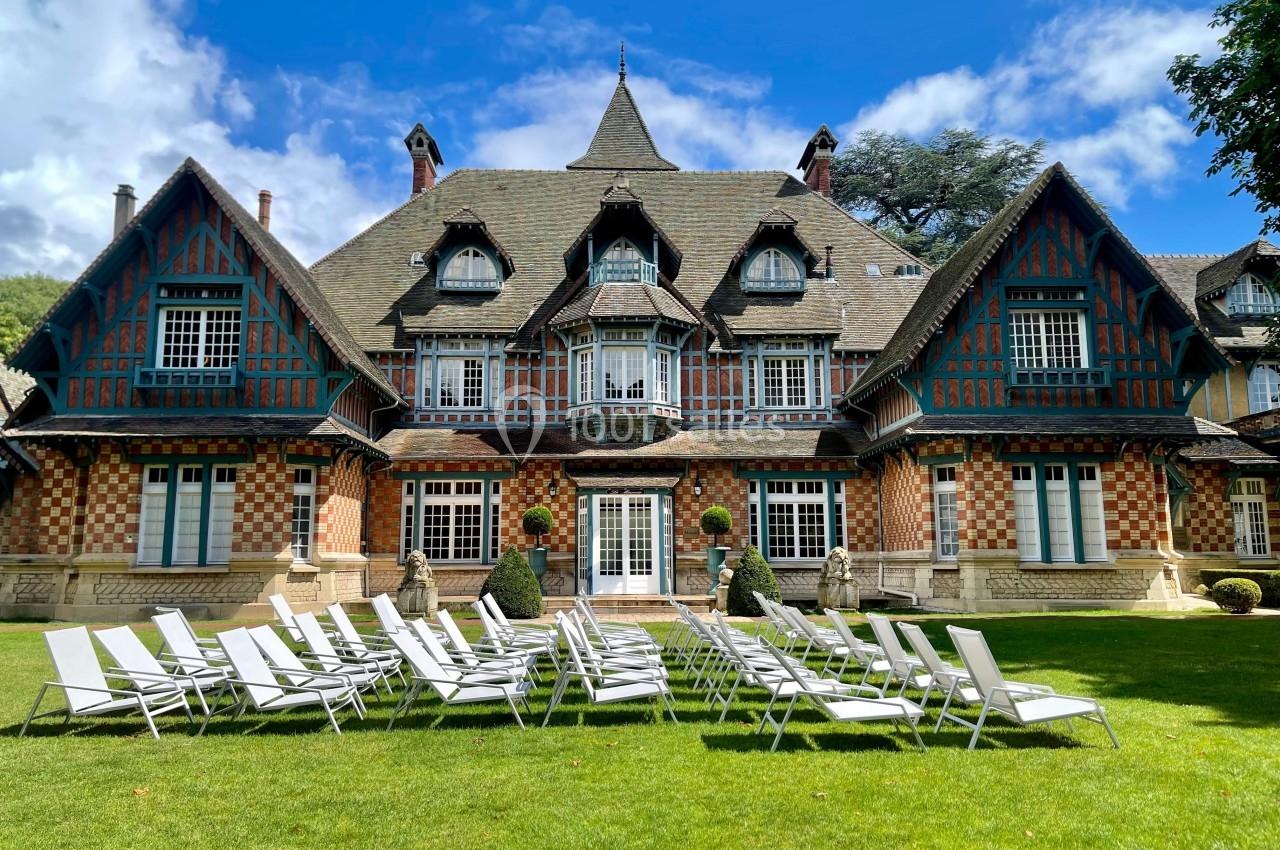 Façade d'une grande maison à colombages avec des chaises longues blanches disposées sur une pelouse.