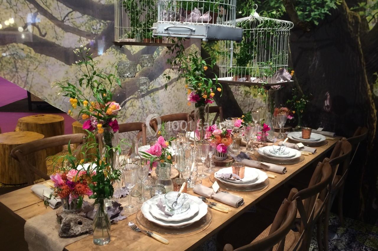Location salle Rueil-Malmaison (Hauts-de-Seine) - Paris Country Club #3 Table en bois décorée avec vaisselle élégante, fleurs colorées et cages à oiseaux suspendues dans un décor naturel.