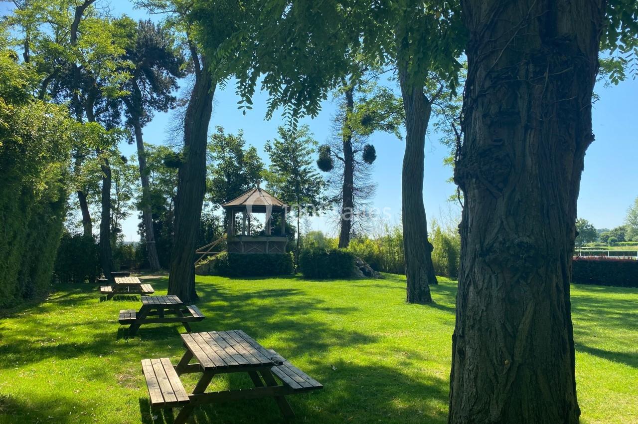 Location salle Rueil-Malmaison (Hauts-de-Seine) - Paris Country Club #4 Espace vert avec tables de pique-nique en bois, arbres ombragés et kiosque au fond sous un ciel dégagé.