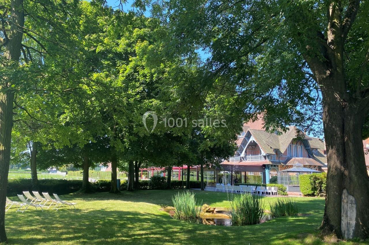 Location salle Rueil-Malmaison (Hauts-de-Seine) - Paris Country Club #2 Jardin arboré avec pelouse, chaises longues, petit étang et bâtiment à colombages en arrière-plan.