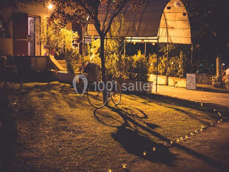 Un vélo posé sur une pelouse éclairée par des lumières tamisées, avec des arbres et une structure en arrière-plan.