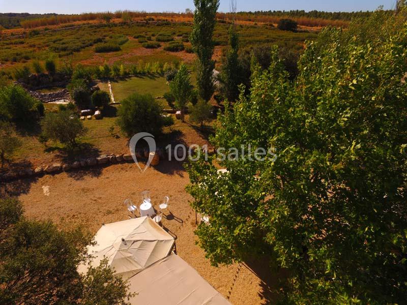 Vue aérienne d'un espace extérieur avec des arbres, une tente beige et une table blanche entourée de chaises.