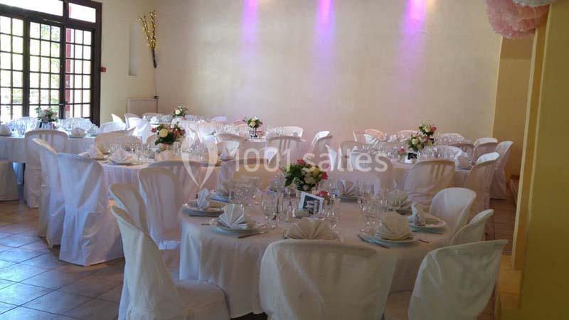 Salle de réception décorée avec des tables rondes dressées, nappes blanches et centres de table fleuris.
