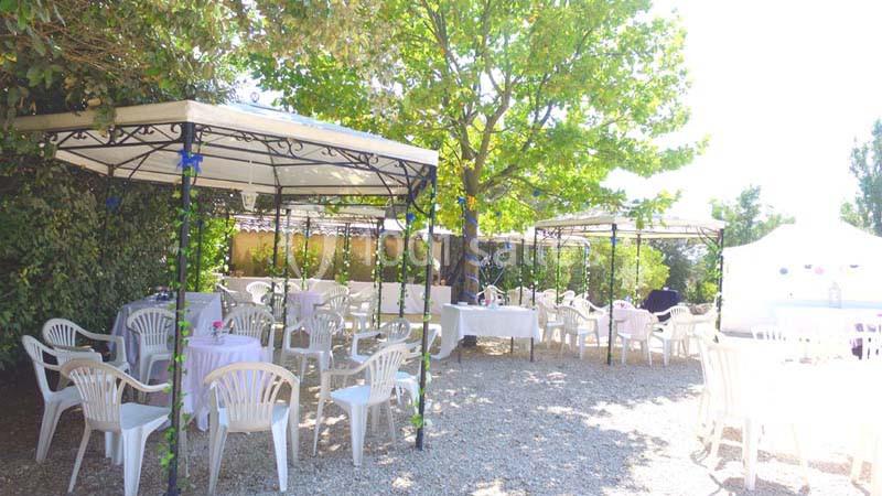 Terrasse extérieure avec tables et chaises en plastique blanc sous des tonnelles, entourée de verdure.