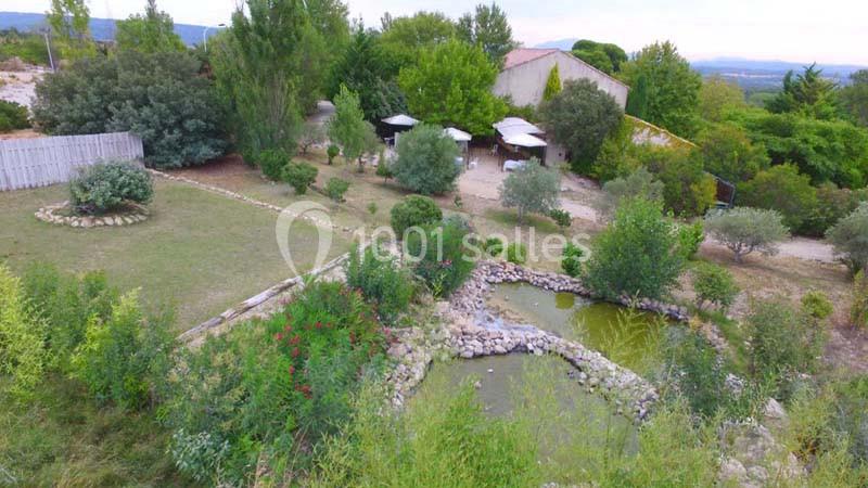 Vue aérienne d'un jardin paysager avec un bassin, des arbres, des arbustes et une maison en arrière-plan.