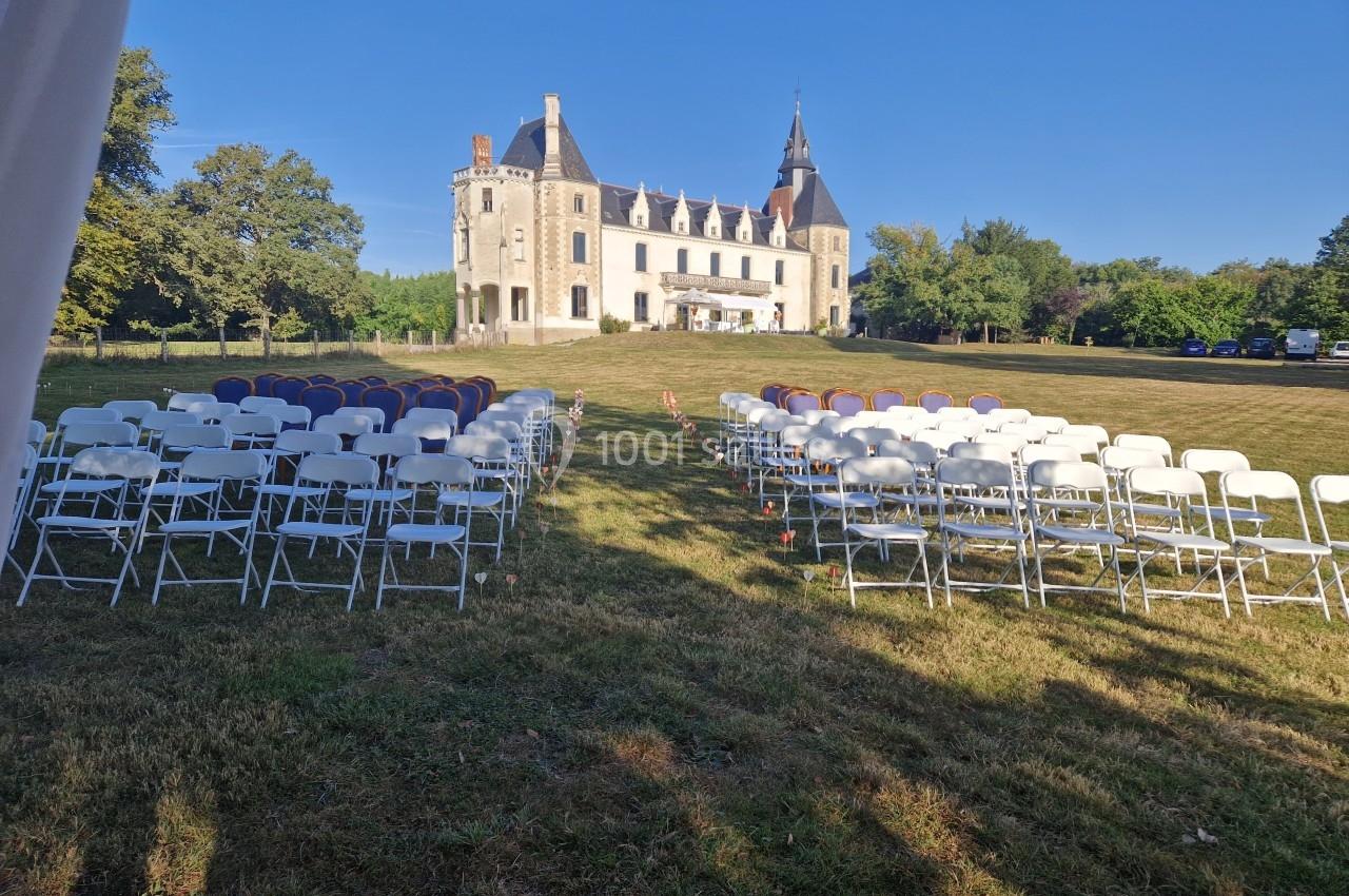 Chaises blanches et violettes disposées en rangées sur une pelouse, face à un château sous un ciel dégagé.