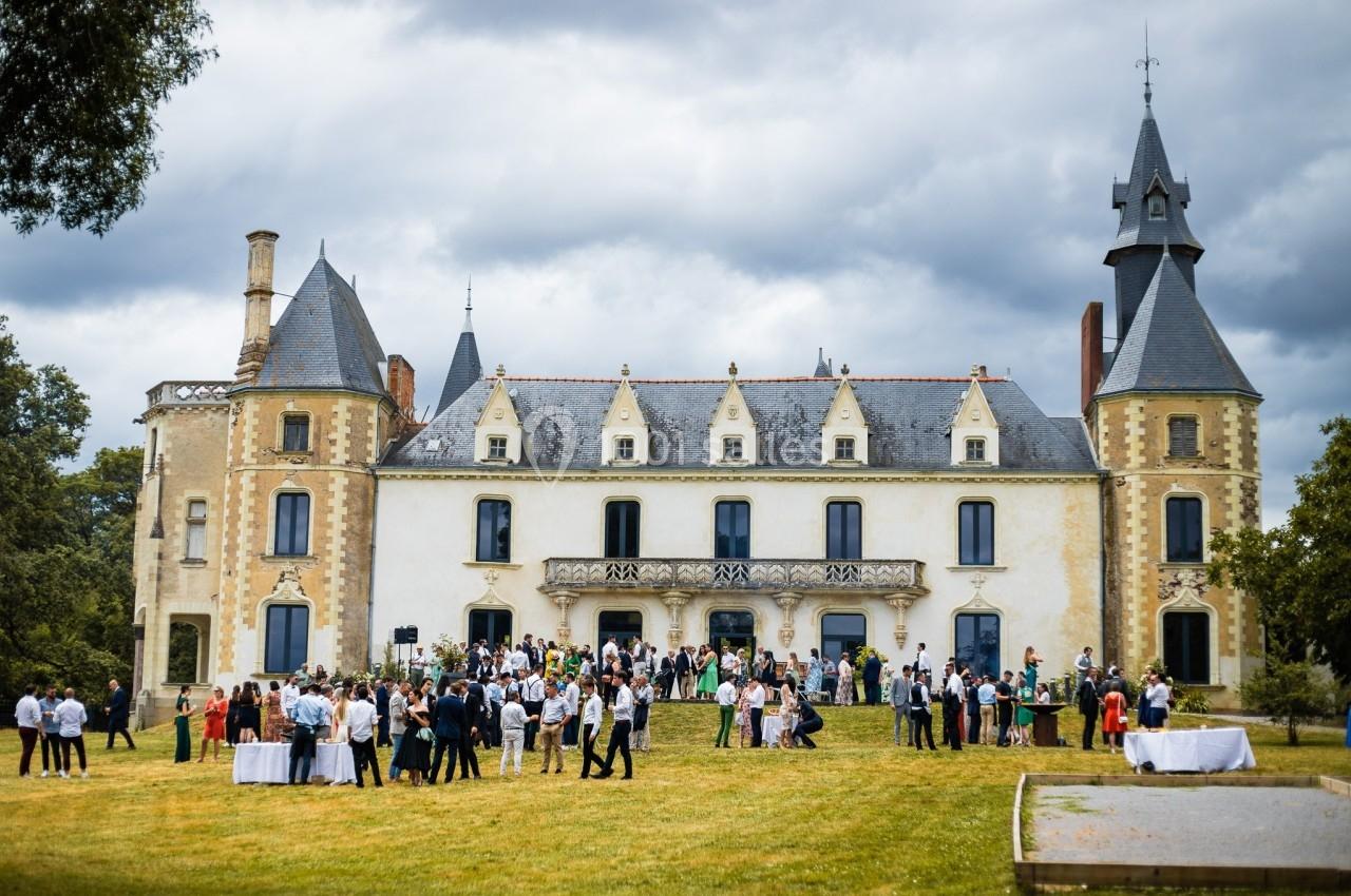 Groupe de personnes rassemblées devant un château à l'architecture traditionnelle sous un ciel nuageux.