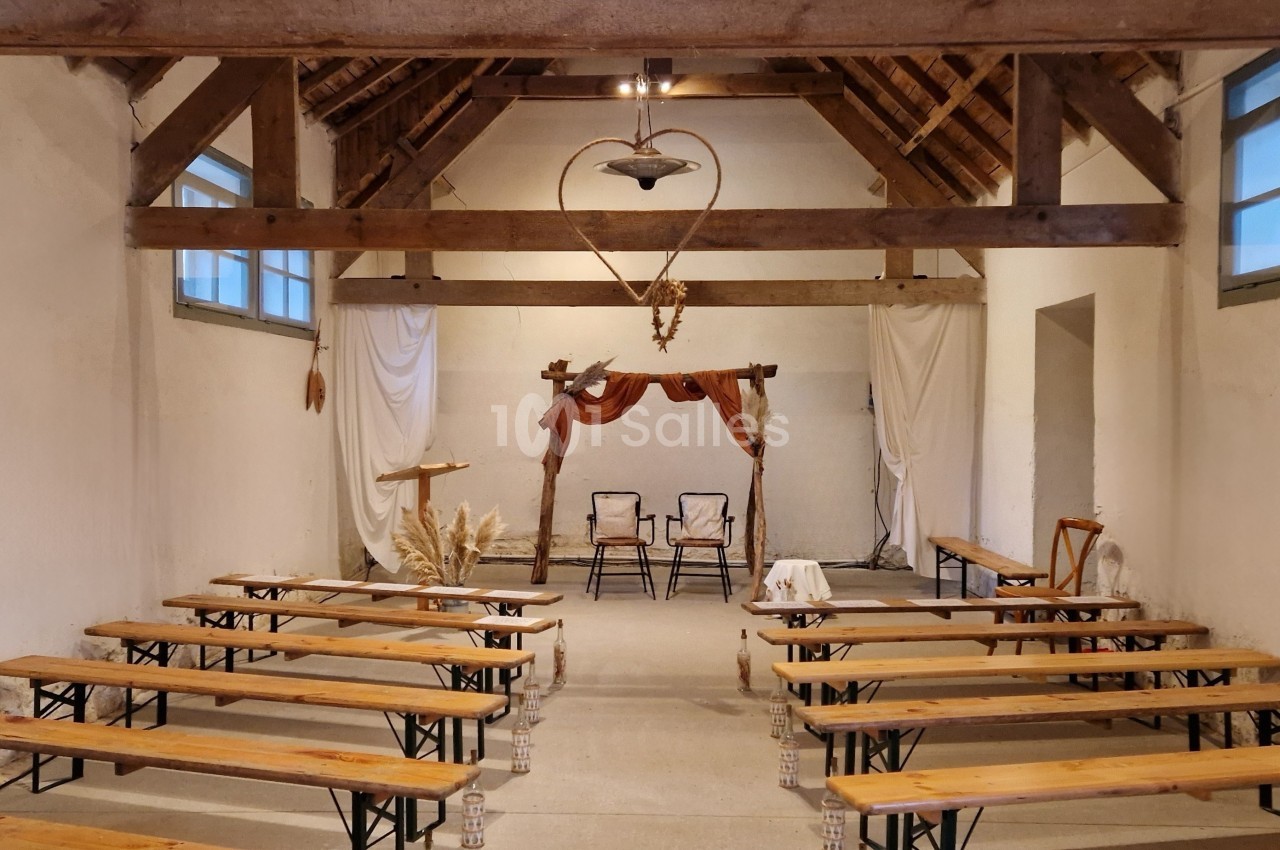 Salle rustique avec bancs en bois, décorée de rideaux blancs et d'un arche en bois ornée de fleurs séchées.