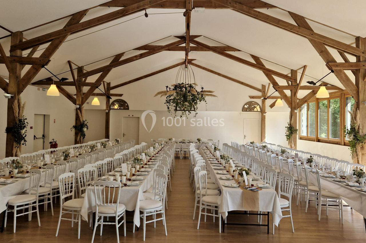 Salle de réception avec de longues tables dressées, décorée de poutres en bois et de suspensions végétales.