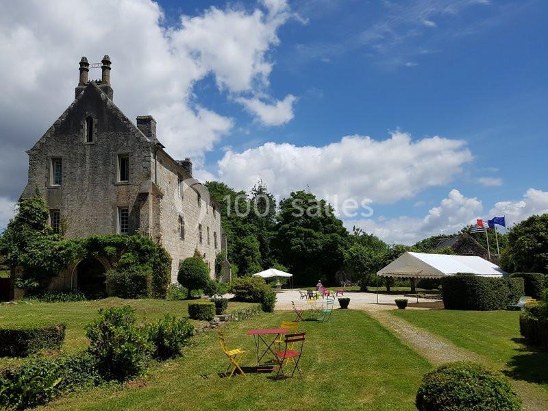 Manoir en pierre entouré de jardins verdoyants, avec une tente blanche et des drapeaux en arrière-plan.