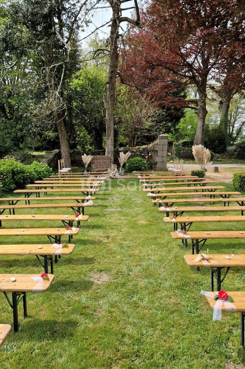 Allée centrale bordée de bancs en bois, décorée pour une cérémonie en extérieur dans un jardin verdoyant.