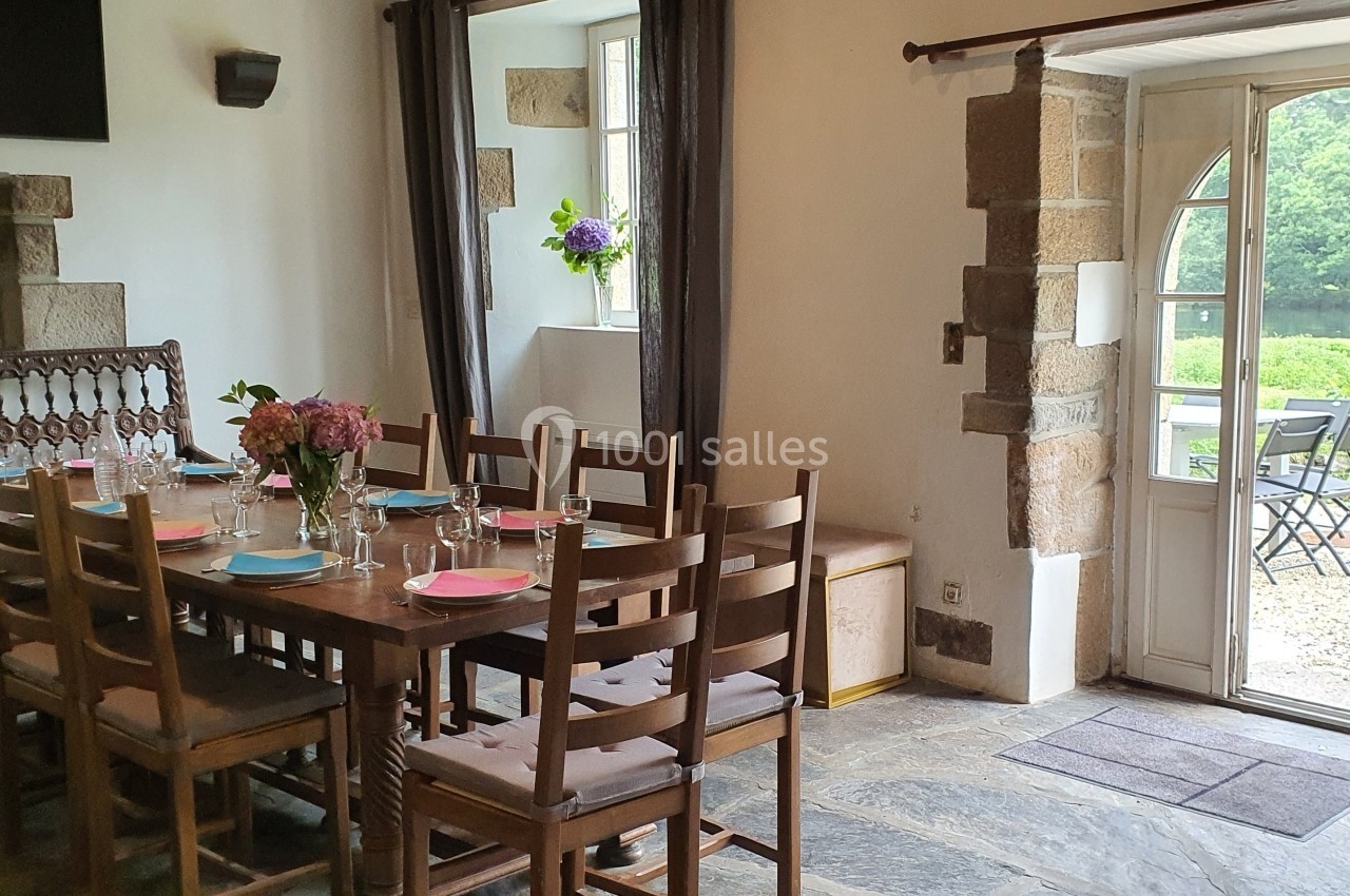 Salle à manger lumineuse avec une grande table en bois, des chaises assorties et une porte ouverte sur un jardin verdoyant.