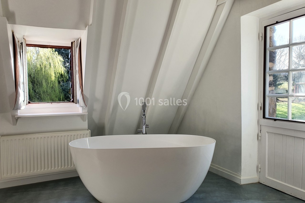 Baignoire blanche moderne dans une salle de bain lumineuse avec fenêtre ouverte sur un jardin verdoyant.