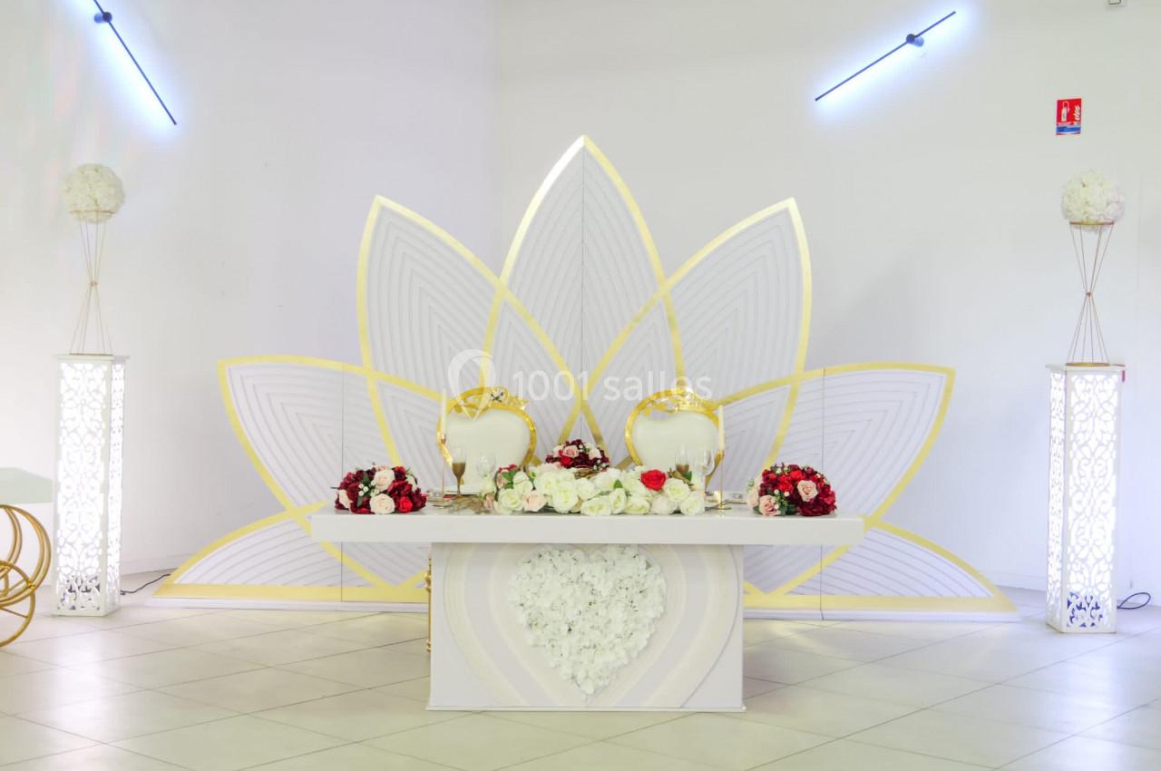Table décorative de mariage avec fleurs rouges et blanches, chaises dorées et fond en forme de pétales dorés et blancs.