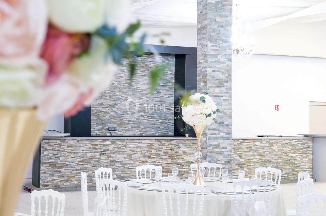 Salle de réception lumineuse avec tables décorées de centres de table fleuris et un mur en pierre en arrière-plan.