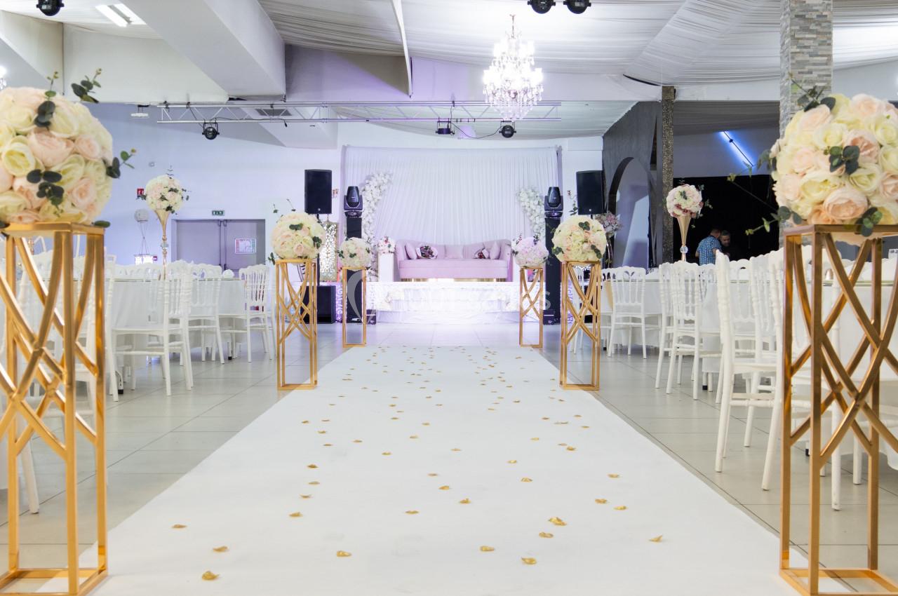 Allée centrale décorée de pétales et de bouquets de fleurs, menant à une scène dans une salle de réception élégante.